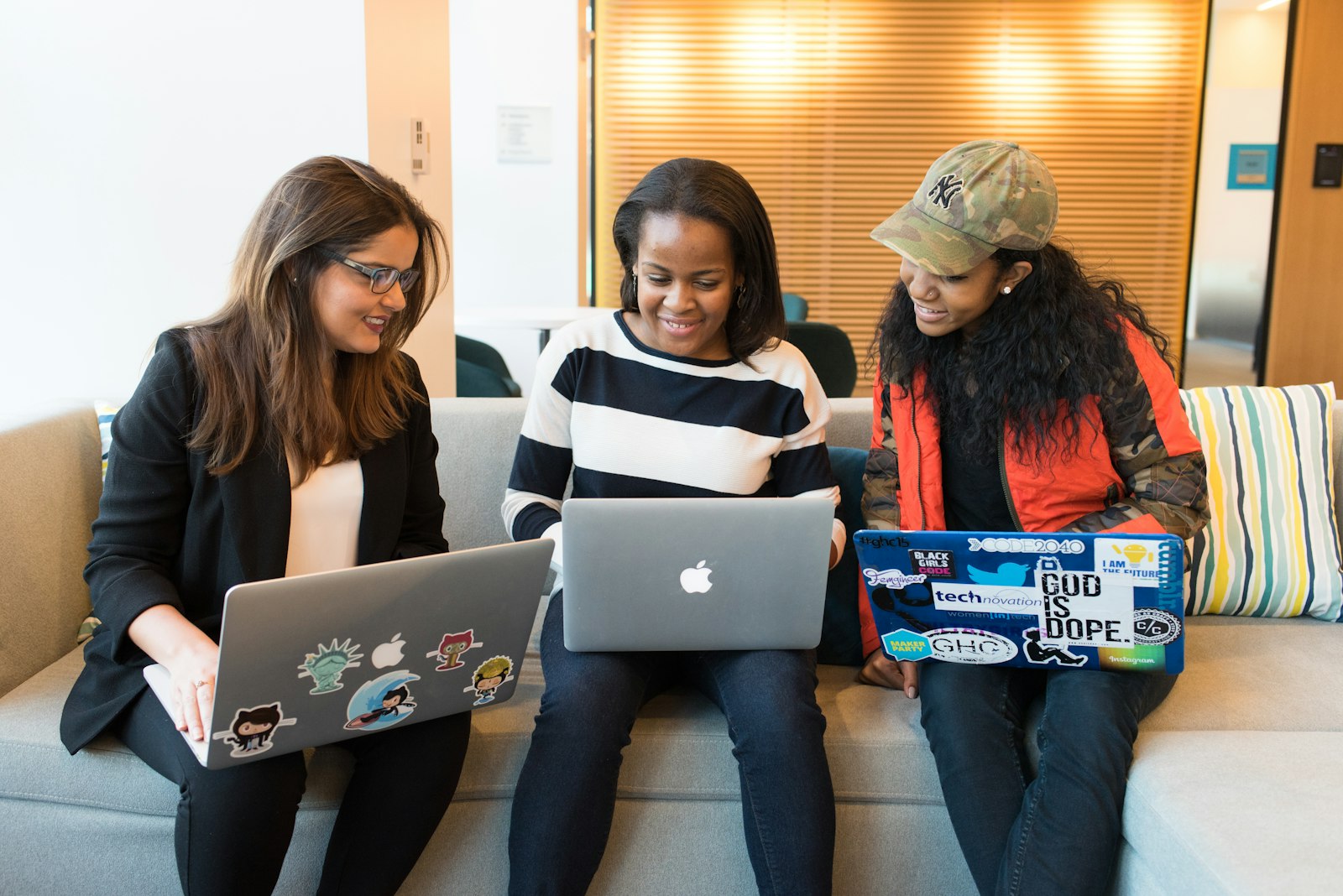 Three women of different backgrounds working on laptops together on a sofa